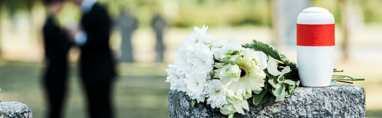 panoramic shot of white flowers and cemetery urn on tombstone